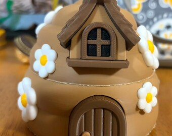 May include: A brown, dome-shaped structure resembling a beehive, decorated with white and yellow daisy-like flowers. It features a dark brown arched door with a small knob and a protruding window frame above it with a black, grid-patterned window.