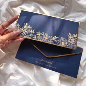 Könnte beinhalten: Marineblaue Einladungskarte mit goldenem Blumendesign und goldenem Rand. Auf der Karte steht "Best Wishes" und die Namen "Raman & Vijay Kapoor". Die rechteckige Karte hat einen passenden Umschlag.