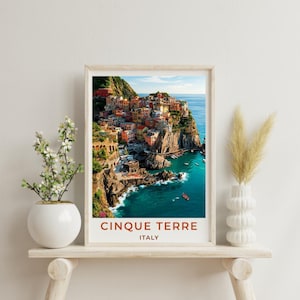 May include: A framed vertical wall art print featuring a colourful coastal landscape of Cinque Terre, Italy, with multi-coloured houses perched on rocky cliffs above a deep blue sea. The text CINQUE TERRE ITALY is printed in red at the bottom.