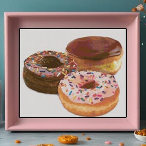 May include: A framed painting of three donuts. One donut is covered in chocolate frosting, another has pink frosting and sprinkles, and the third has chocolate frosting and colorful sprinkles. The painting is in a pink frame.