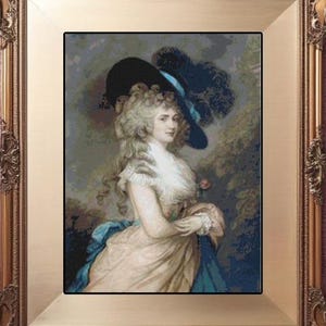 Op de afbeelding: Een ingelijst portret van een vrouw in een periodejurk en hoed. Het portret staat in een gouden, sierlijke lijst. De vrouw draagt een grote zwarte hoed met blauwe accenten en een witte jurk. De achtergrond is gedempt groen en blauw.