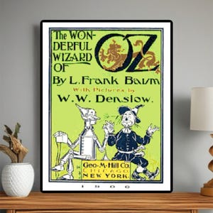 May include: A framed vintage book cover for "The Wonderful Wizard of Oz" by L. Frank Baum, with illustrations by W.W. Denslow. The cover features the title in green and black, with illustrations of the Tin Man and Scarecrow.