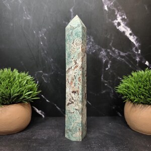May include: A tall, six-sided crystal tower with a pointed top. The stone features a marbled pattern of seafoam green, white, and earthy brown tones throughout its polished surface, displaying natural mineral inclusions and varied color textures.