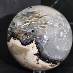 Peut inclure: Une sph&egrave;re polie aux couleurs vari&eacute;es, notamment grise, blanche, noire et marron. La sph&egrave;re pr&eacute;sente un aspect marbr&eacute; avec des motifs et des textures complexes. L'ensemble sugg&egrave;re un objet d&eacute;coratif ou une pierre pr&eacute;cieuse.