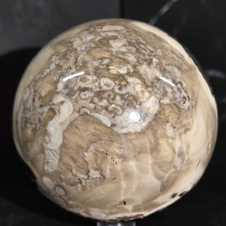 Peut inclure: Une pierre sph&eacute;rique polie, pr&eacute;sentant un motif tourbillonnant de teintes beige, cr&egrave;me et marron. La surface a une finition brillante, refl&eacute;tant la lumi&egrave;re. La pierre semble &ecirc;tre un objet d&eacute;coratif ou un sp&eacute;cimen naturel.