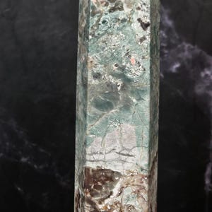 May include: A tall, hexagonal crystal tower featuring a polished surface with a marbled appearance. The stone displays a blend of pale mint green, deep forest green, and earthy brown tones, characterized by intricate white veining and fissures.