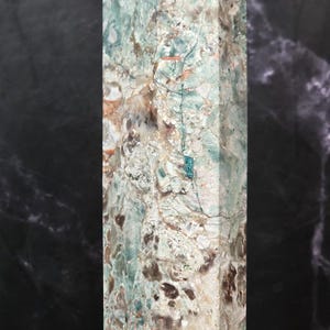 May include: A tall, rectangular stone pillar featuring a complex, multi-colored mineral pattern. The surface displays a mix of pale green, white, brown, and dark grey inclusions with a polished finish, showcasing natural crystalline textures.