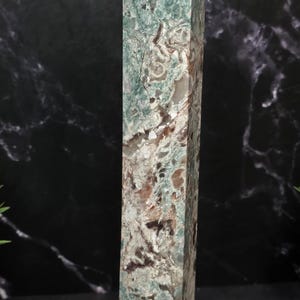 May include: A tall, rectangular stone obelisk featuring a complex, marbled pattern of sage green, cream, and dark brown mineral inclusions. The surface displays a polished finish with visible natural veining and crystalline textures throughout.