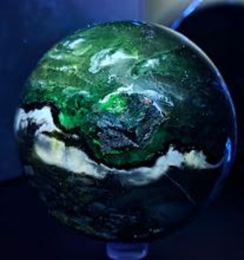 Peut inclure: Une sph&egrave;re polie avec un motif tourbillonnant de verts profonds, de blancs et de noirs. Le globe en pierre pr&eacute;cieuse a une finition brillante, avec des zones de couleurs claires et sombres contrast&eacute;es. La sph&egrave;re est pr&eacute;sent&eacute;e sur un petit socle transparent.