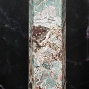 May include: A tall, hexagonal stone tower featuring a complex, marbled surface with a blend of pale mint green, earthy brown, and creamy white tones. The polished mineral structure displays intricate natural veining and fractured patterns.