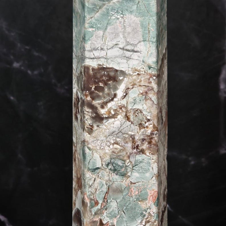 May include: A tall, hexagonal stone tower featuring a complex, marbled surface with a blend of pale mint green, earthy brown, and creamy white tones. The polished mineral structure displays intricate natural veining and fractured patterns.