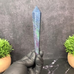 May include: A tall, faceted crystal tower featuring a blend of deep blue, vibrant magenta, and bright green mineral inclusions. The stone has a smooth, polished surface with a pointed hexagonal top, showcasing natural color variations throughout.