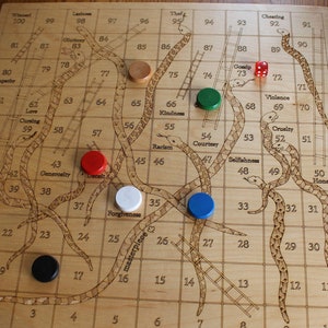 Könnte beinhalten: Ein hölzernes Spielbrett mit einem Schlangen-und-Leitern-Design. Das Brett hat ein Gitter aus Feldern mit den Zahlen von 1 bis 100. Auf dem Brett sind Schlangen und Leitern gezeichnet, und es befinden sich vier Spielsteine auf dem Brett. Die Spielsteine sind rot, blau, grün und weiß.