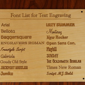 May include: A rectangular light-colored wooden plaque featuring the engraved title Font List for Text Engraving. The board displays two columns of various font names, including Arial, Bellota, Daggersquare, Engravers Roman, Freestyle Script, Gabriola, Goudy Old Style, Jackport Regular, Jumiko, Lazy Summer, Monterey, New Rocker, Open Sans Con., Playbill, Sunday, The Goldsmith Regular, Times New Roman, and Script MJ Bold.