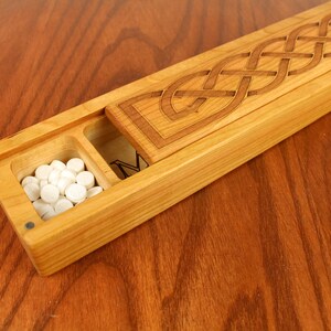 May include: A wooden box with a Celtic knot design on the lid. The box has a small compartment with white pills inside.