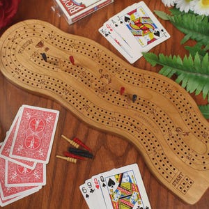 May include: A wooden cribbage board with a wavy, elongated shape featuring numbered tracks, a start and finish point, and small holes for pegs. The board includes red and black plastic pegs, along with several standard playing cards.