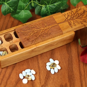 May include: A wooden pill box with a sliding lid, featuring a carved tree design. The box is divided into compartments, some containing pills. The letters "S" and "M" are visible. The box is on a wooden surface, with pills arranged in floral patterns.