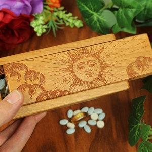 May include: Wooden pill box with a sun and clouds design. The box has two compartments labelled "S" and "M".