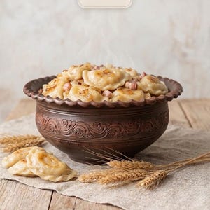 May include: A dark brown ceramic bowl with a scalloped rim and embossed scroll patterns, filled with steamed dumplings topped with bacon bits and caramelized onions. A tag above reads HANDMADE IN UKRAINE with a trident symbol.
