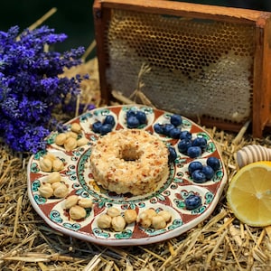 Peut inclure: Nature morte rustique avec une assiette décorative garnie d'une pâtisserie en forme d'anneau, de myrtilles et de noix. Un bouquet de lavande, un rayon de miel, une moitié de citron et une bougie sont également présents, sur de la paille.