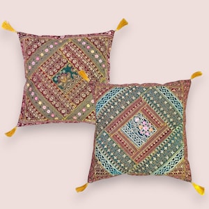 Op de afbeelding: Twee vierkante decoratieve kussens met ingewikkelde geborduurde patronen in tinten bordeauxrood, blauwgroen en goud. Elk kussen heeft een centraal ruitontwerp en is versierd met gele kwastjes in elke hoek. De kussens zijn waarschijnlijk voor woondecoratie.