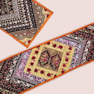 May include: Two decorative table runners with intricate floral and geometric patterns in burgundy, gold, and purple. The runners have an orange border and are made from embroidered fabric. The text in the image says, "NOTE - These Table Runners/Wall Hangings Are Made From Random Embroidery Border..."