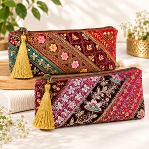 Peut inclure: Deux trousses rectangulaires à fermeture éclair en velours ornées de broderies complexes, de paillettes et de fils métalliques dans des tons de rouge, rose, bleu sarcelle et or. Chaque trousse possède une longue tirette à pompon doré.