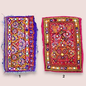 Può includere: Due toppe tessili ricamate e colorate. Una è principalmente viola con dettagli gialli, rossi e bianchi. L'altra è rossa con accenti gialli, neri e bianchi. Entrambe presentano motivi intricati e abbellimenti a specchio.