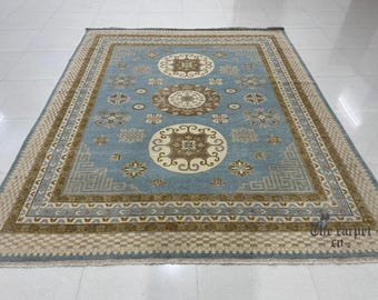 May include: A rectangular, light blue rug with an intricate pattern. The rug features a central design of large, circular medallions in shades of brown and cream, surrounded by floral and geometric motifs. The border is a mix of beige, brown, and blue.