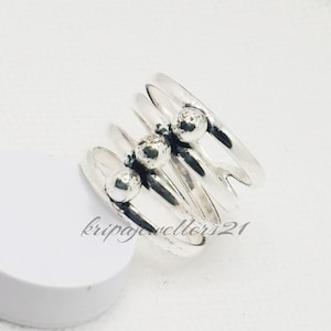 May include: A silver ring with a distinctive design. The ring has multiple bands, each with a small, round bead. The bands are arranged in a layered style, creating a textured and eye-catching look. The ring is likely made of sterling silver.