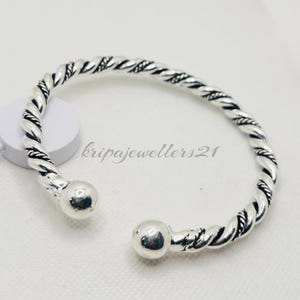 Puede incluir: Un brazalete plateado con un diseño de cuerda trenzada. La pulsera tiene una bola redondeada en cada extremo. El texto "kripajewellers21" es visible en el fondo.