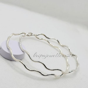 May include: Two silver bangles with a wavy design. The bangles are displayed on a white surface. The text "kripajewellers21" is visible on the surface.