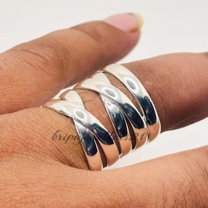 Peut inclure: Une bague argentée avec un design à plusieurs bandes. La bague s'enroule autour du doigt avec une série de bandes entrelacées, créant un aspect texturé et accrocheur. La bague est en métal brillant et réfléchissant.