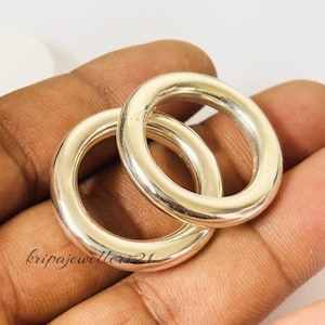 Könnte beinhalten: Zwei silberfarbene, kreisförmige Ringe. Die Ringe haben eine glatte, glänzende Oberfläche und eine abgerundete Form. Sie werden auf einer hautfarbenen Oberfläche präsentiert. Der Text "kripajeweller21" ist sichtbar.