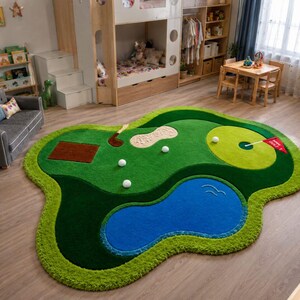 May include: A large, irregularly shaped area rug designed to look like a golf course. The rug features a green fairway, a blue water hazard, a tan sand bunker, a brown tee box, a light green putting green with a red flag, and white golf balls.
