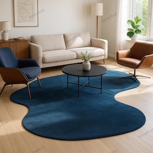 Può includere: Un grande tappeto blu scuro dalla forma irregolare domina il centro della stanza. Il design unico del tappeto aggiunge un tocco moderno allo spazio abitativo. Un tavolino nero è posizionato sul tappeto, circondato da un divano beige e due poltrone.