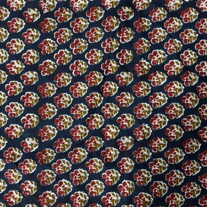 May include: Close-up of a fabric with a repeating floral pattern. The design features clusters of red and white flowers with green leaves on a dark blue background. The fabric is likely cotton or a similar material.