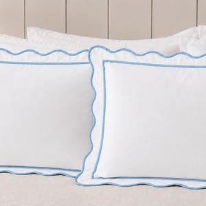 May include: Two rectangular white pillow shams featuring a scalloped edge border outlined in light blue piping. The design includes a central rectangular panel framed by a matching light blue line, creating a clean and structured appearance.