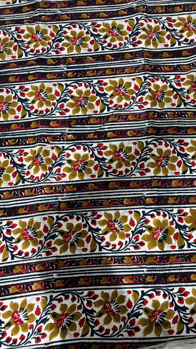 May include: Floral fabric with a repeating pattern of stylized flowers in gold, red, and navy blue on a white background. The design includes horizontal stripes with floral and geometric elements.
