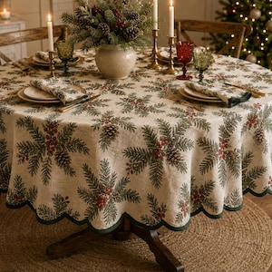 May include: A round beige tablecloth featuring a repeating pattern of green pine branches, brown pinecones, and red berries, finished with a scalloped dark green edge. The fabric is draped over a circular wooden table set with plates and napkins.