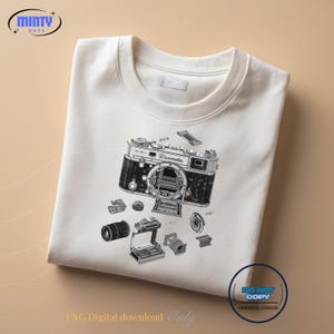 May include: White crewneck sweatshirt featuring a detailed black and white illustration of a vintage camera with its components. The design includes the word "Peemda" on the camera body. The sweatshirt also has the text "PNG Digital download Only" and "DO NOT COPY ORIGINAL DESIGN".