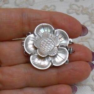 May include: A multi-strand jewelry clasp crafted from iridescent mother-of-pearl, shaped like a five-petaled flower with a textured center. The silver-toned metal hardware features multiple loops on the sides for attaching jewelry strands.