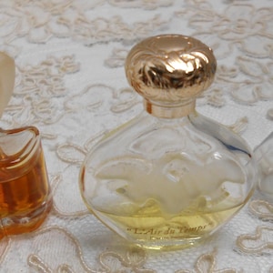 May include: Three vintage perfume bottles. One is a star-shaped bottle with an orange liquid and a frosted flower-shaped stopper. The second is a round bottle with a gold-colored top and a design on the front. The third is a triangular bottle with a blue stopper.