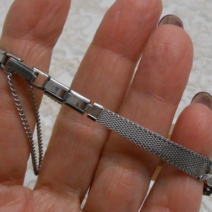 May include: A silver watch band with a mesh design and a clasp closure. The band is made of metal and has a polished finish.