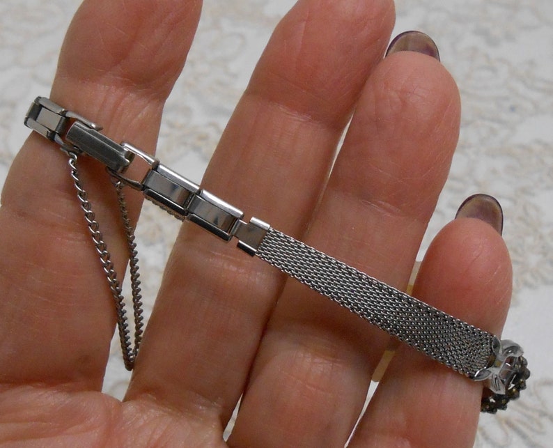 May include: A silver watch band with a mesh design and a clasp closure. The band is made of metal and has a polished finish.