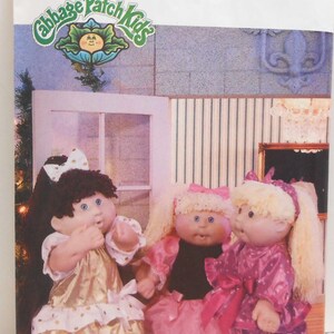 May include: A vintage sewing pattern for Cabbage Patch Kids dolls. The pattern is for making three different outfits for the dolls. The dolls are wearing a gold dress, a pink dress, and a purple dress. The pattern is from Butterick and is size 5200.