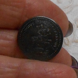 Könnte beinhalten: Eine dunkle, kreisförmige Münze mit geprägtem Text und einem königlichen Emblem. Die Oberfläche der Münze scheint gealtert zu sein, mit sichtbaren Abnutzungserscheinungen. Der Text enthält das Jahr 1973. Die Münze wird zwischen Fingern gehalten.