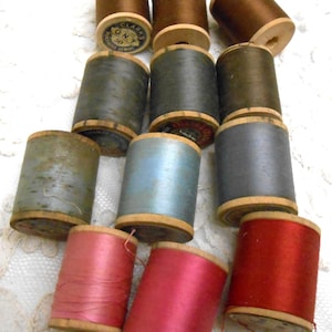 May include: A collection of vintage wooden spools filled with colorful thread. The spools are in various shades of brown, gray, blue, pink, and red. Some spools have labels with text. The thread appears to be silk or a similar material.