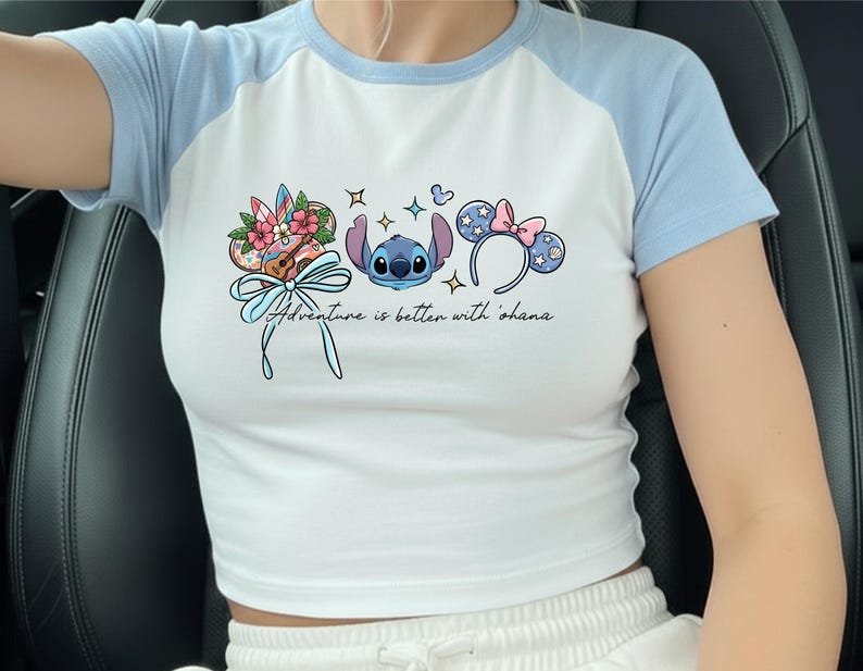 A person wearing a white and blue cropped top with a graphic design featuring a character from the Disney movie Lilo and Stitch, along with various Disney-themed elements such as flowers and earmuffs.