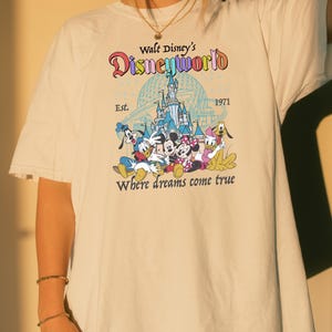 A person wearing a white t-shirt with a Disney World logo and text printed on it.